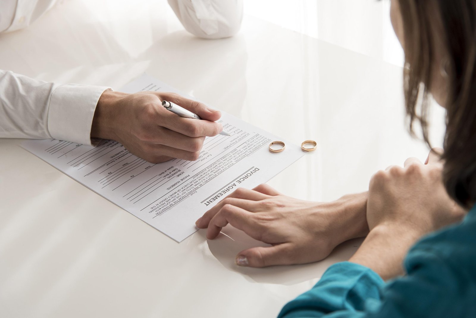 Foto de un abogado asesorando a una mujer con sus dos anillos sobre la mesa al lado del papel de divorcio
